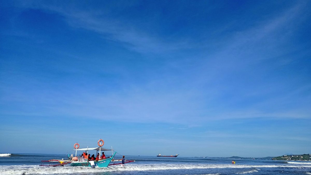 A small boat with a lifebuoy navigates the vibrant blue ocean under a clear sky.