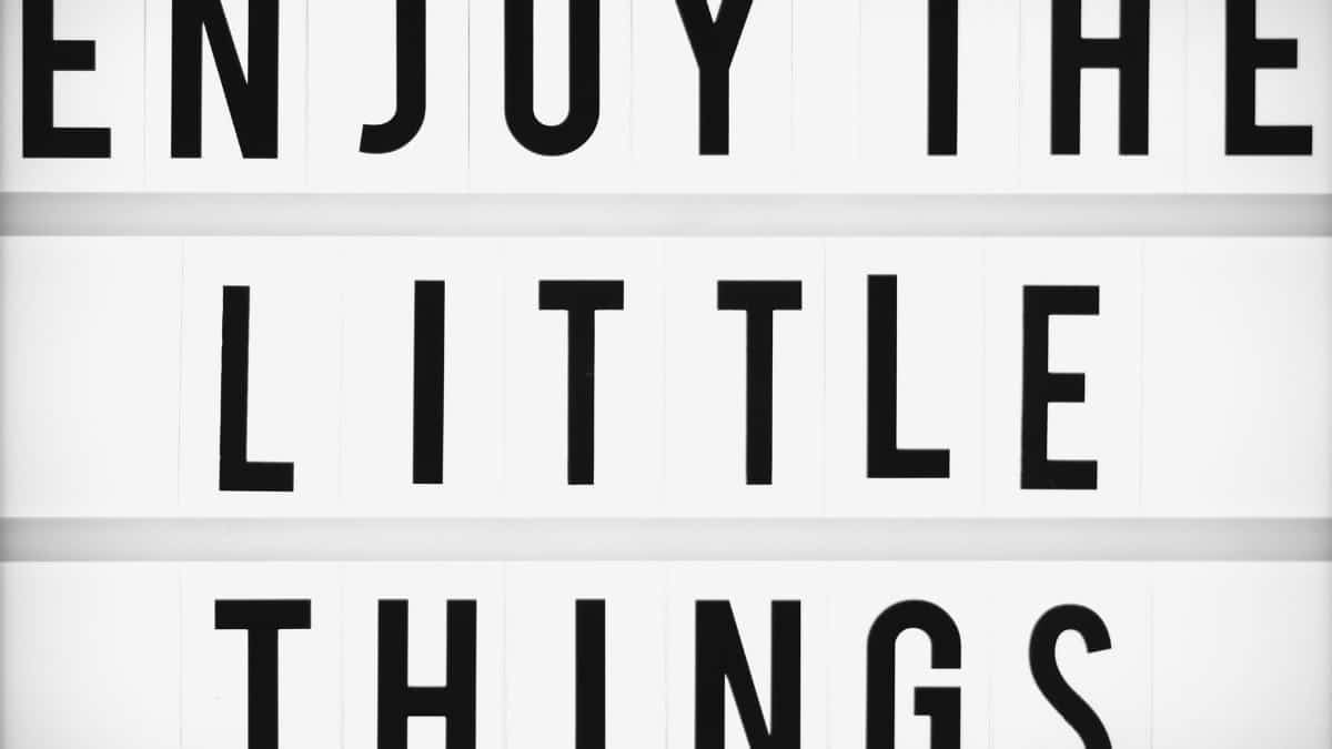 Minimalist design of the inspirational quote 'Enjoy The Little Things' displayed on a lightbox.