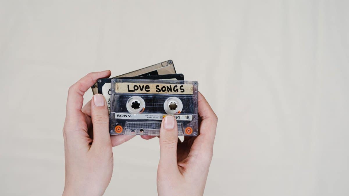 Hands holding vintage cassette tapes, including a 'Love Songs' label, evoking nostalgia.