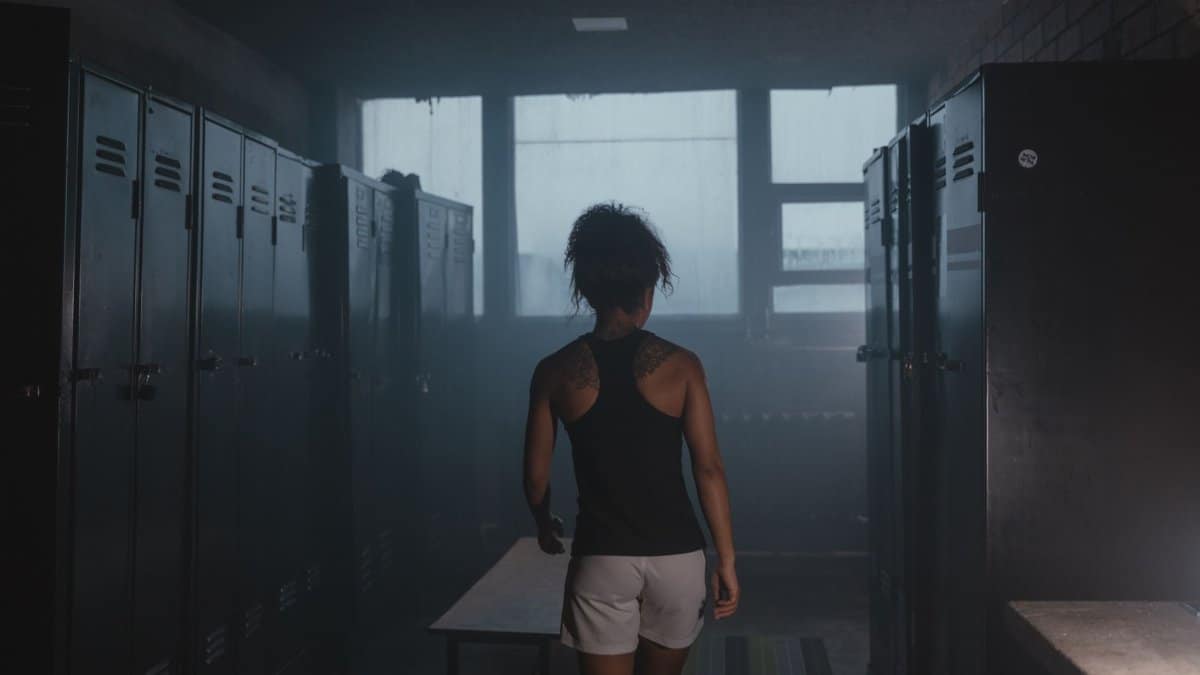 A woman in sports attire walks through a dimly lit locker room, creating a moody atmosphere.