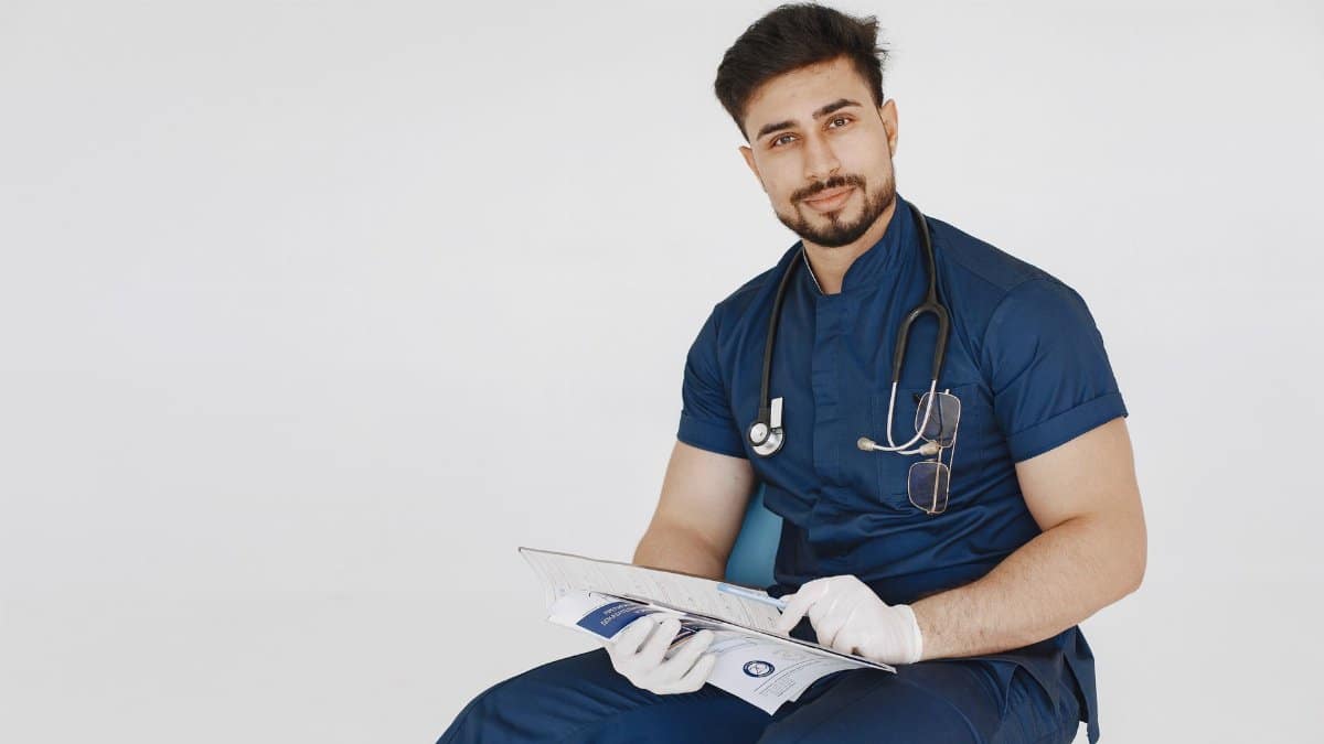 Young male doctor in blue scrubs reviewing medical records with a confident smile.