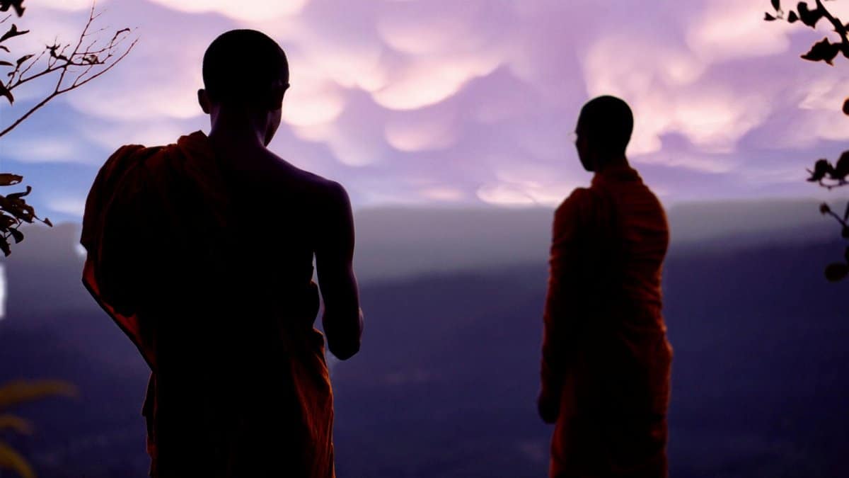 Two monks stand in contemplation at sunset, promoting spirituality and meditation.