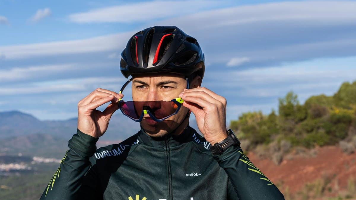 Adult male cyclist adjusting sunglasses outdoors, emphasizing sport and style.