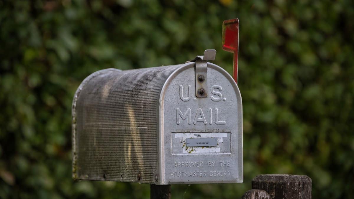 A traditional U.S. mailbox with red flag against a lush green blurred background.