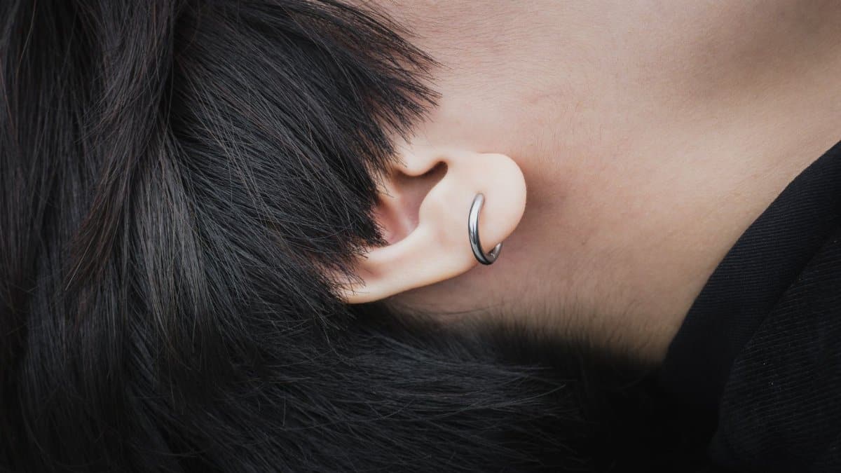Detailed close-up of an ear featuring a silver hoop earring and black hair.