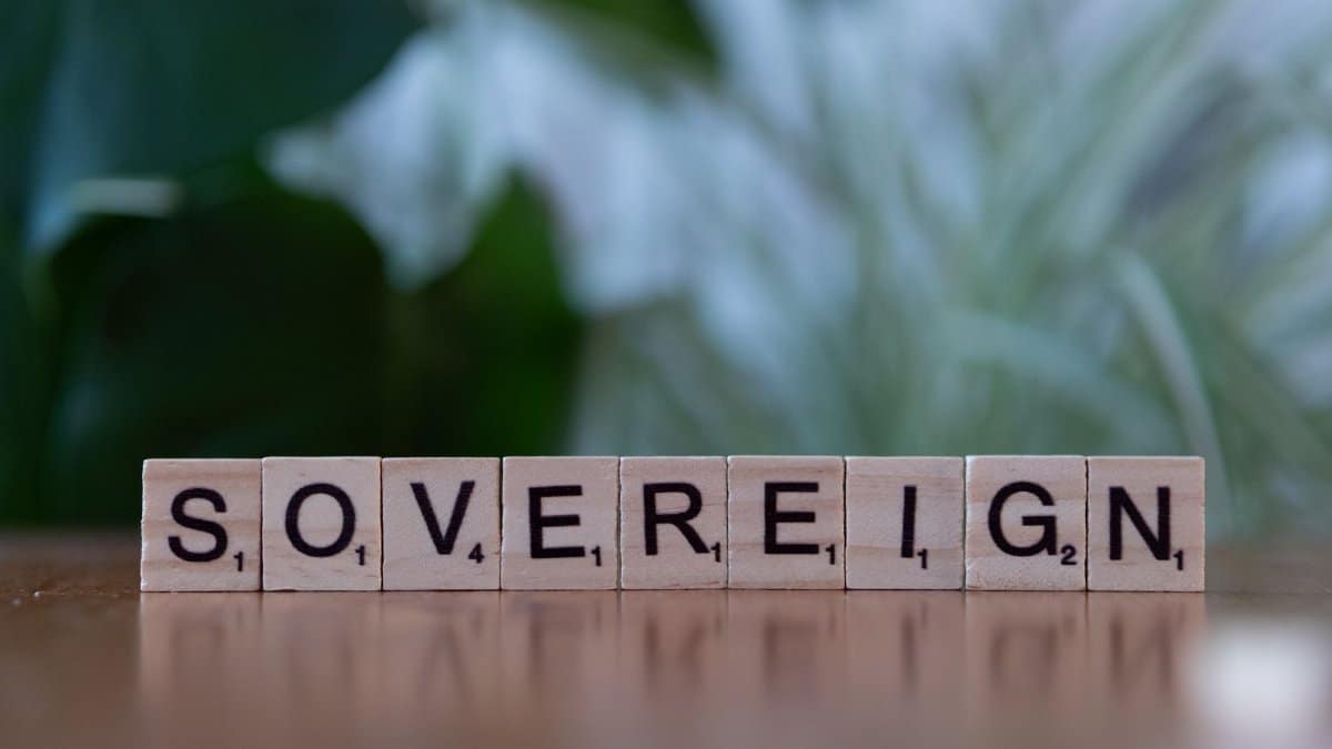 Close-up of wooden Scrabble tiles spelling 'sovereign' on a table with blurred green background.