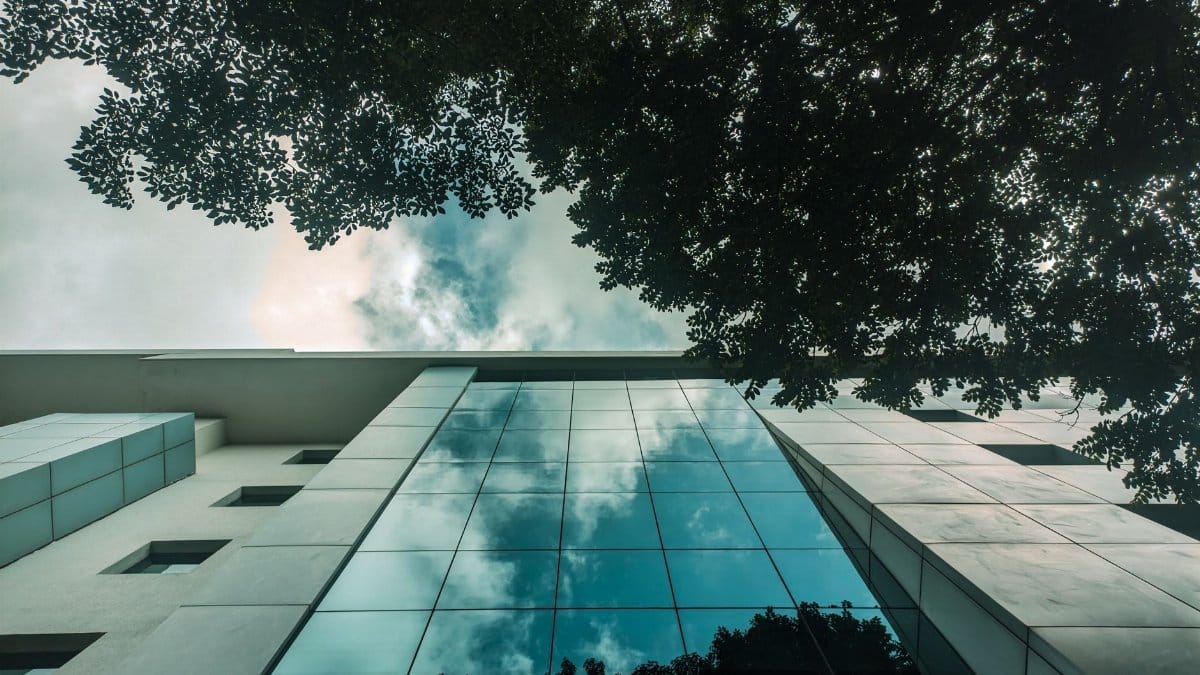 Sky and trees beautifully reflected in the glass facade of a modern building.