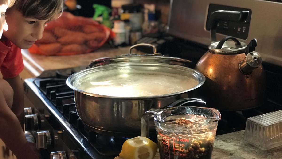 A child curiously watches a pot on the stove in a cozy kitchen setting.