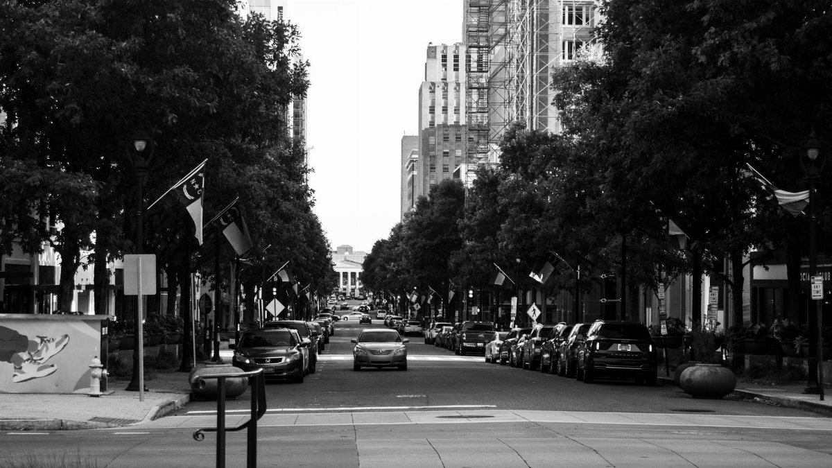 Black and white view of a bustling Raleigh city street with parked cars and flags.