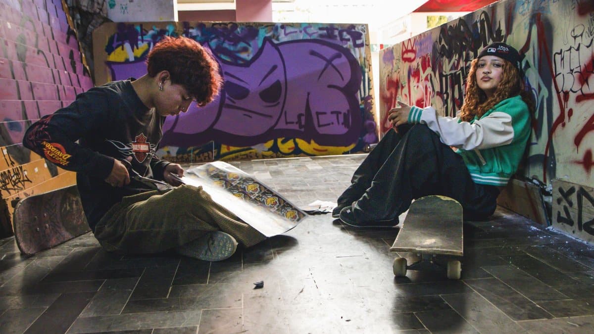 Two young skateboarders relax in a graffitied alley, capturing urban street culture.