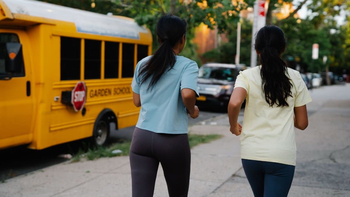 Two women jogging on a sidewalk past a yellow school bus on a summer day.