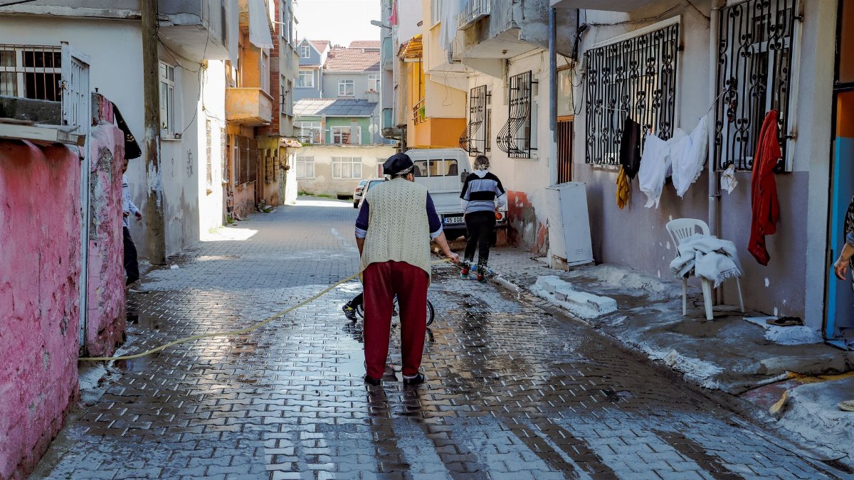 Two people clean a wet street in an urban neighborhood of Tekirdağ, Türkiye.