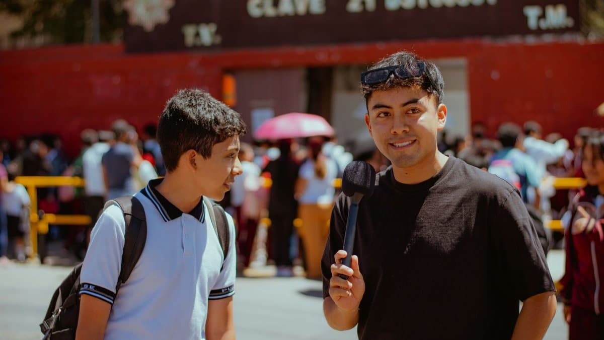 Man holding microphone interacting with a student outside a school building.