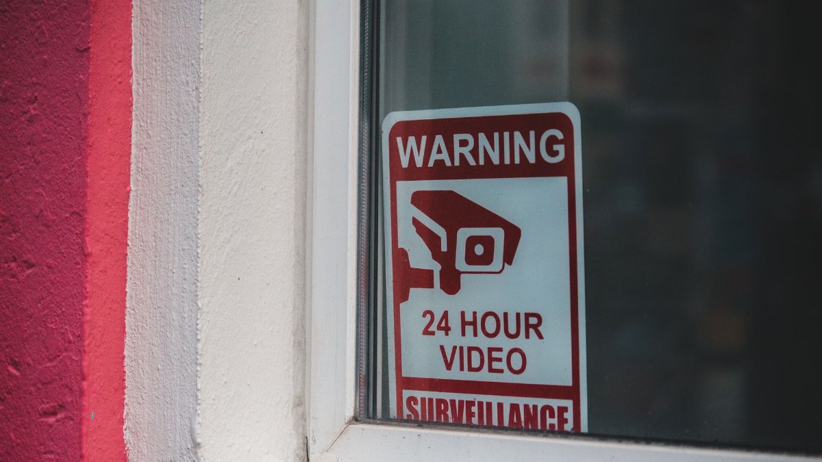 Red warning sign of video surveillance placed behind window of building in daytime