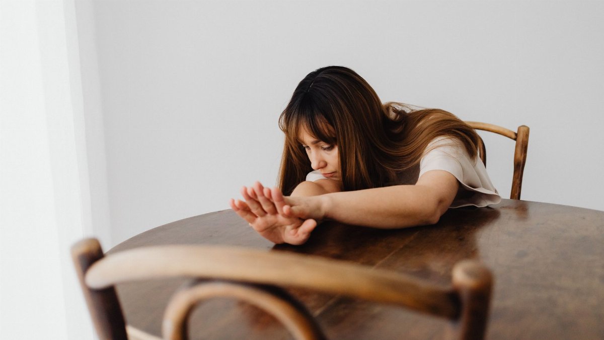 A woman sits at a table resting her arms, creating a somber and contemplative mood.
