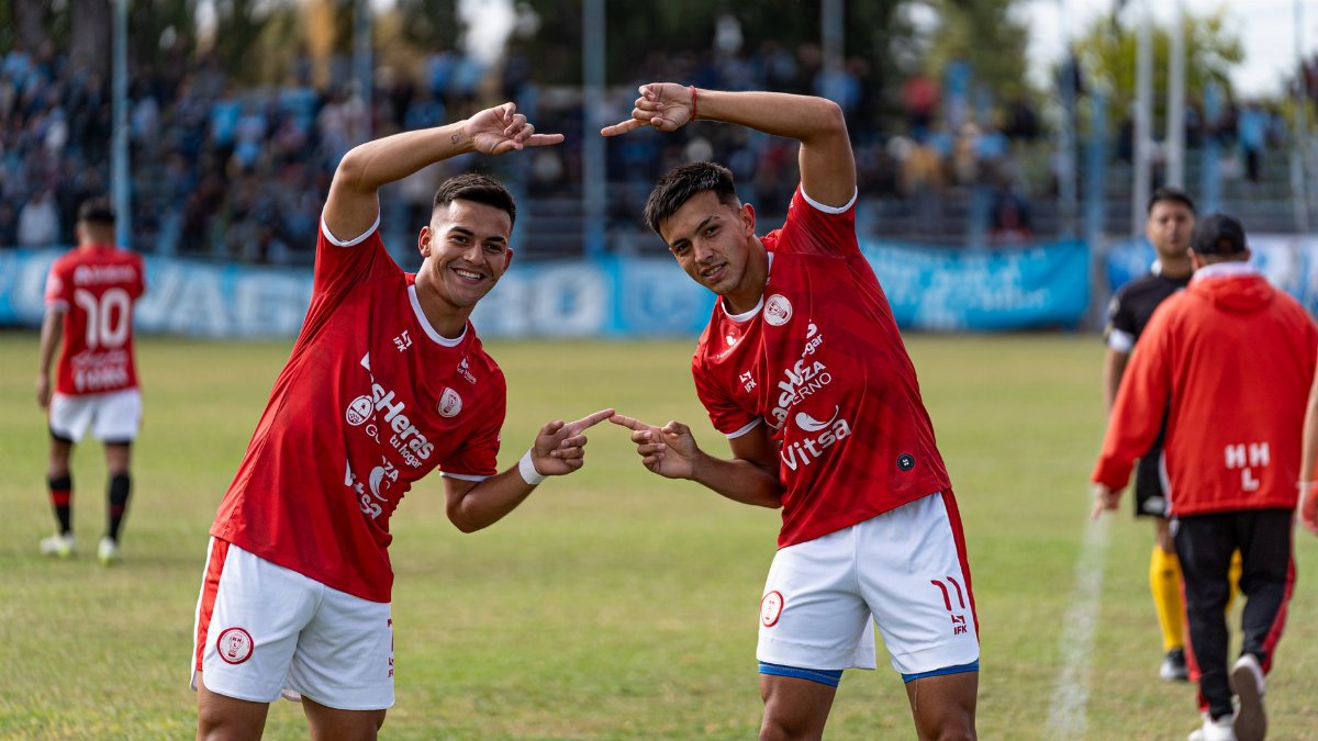 Two young male soccer players celebrate on the field in bright sunlight.