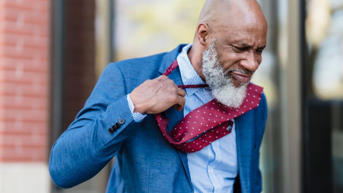 Senior man in blue suit adjusting tie with an expressive look outdoors.
