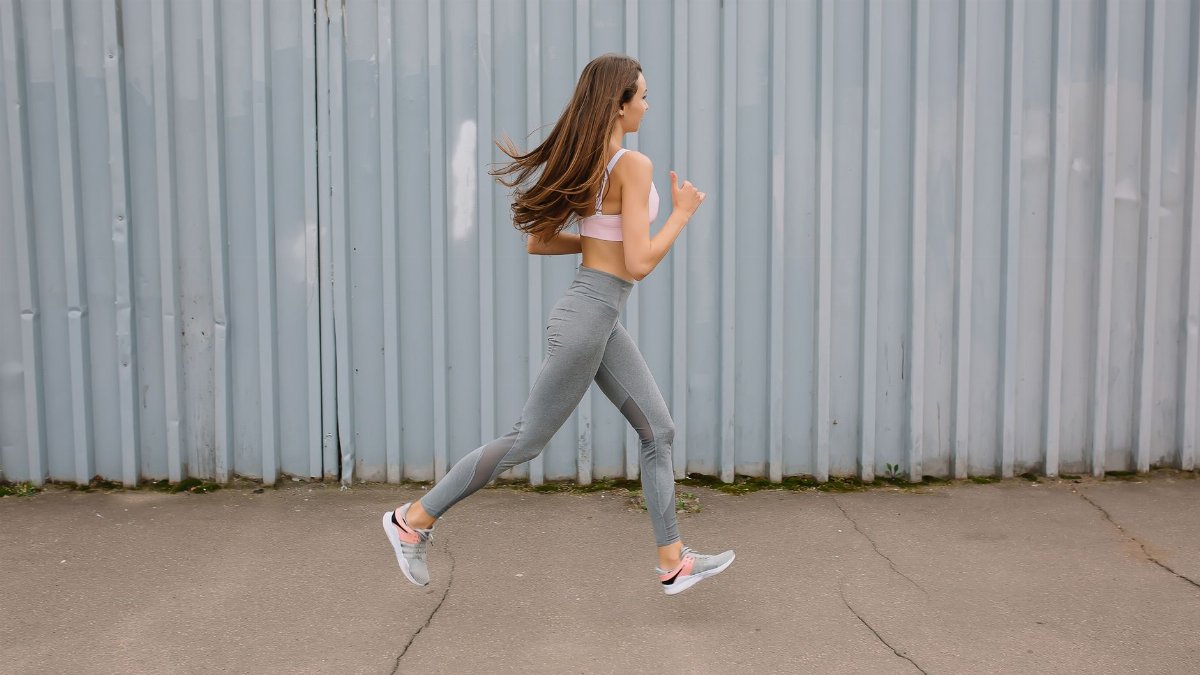 Fit woman running outdoors in activewear with sports bra and leggings. Motion captured at day time.