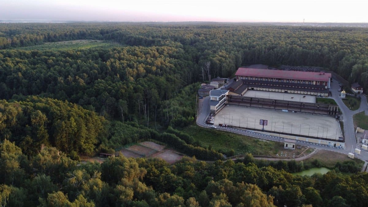 Aerial view of a sports complex amidst lush forest in Leninsky District, Russia.