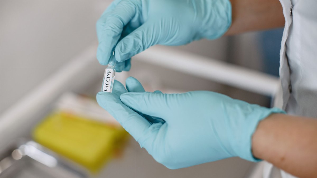 Close-up of hands in gloves holding a vaccine vial in a clinical setting.
