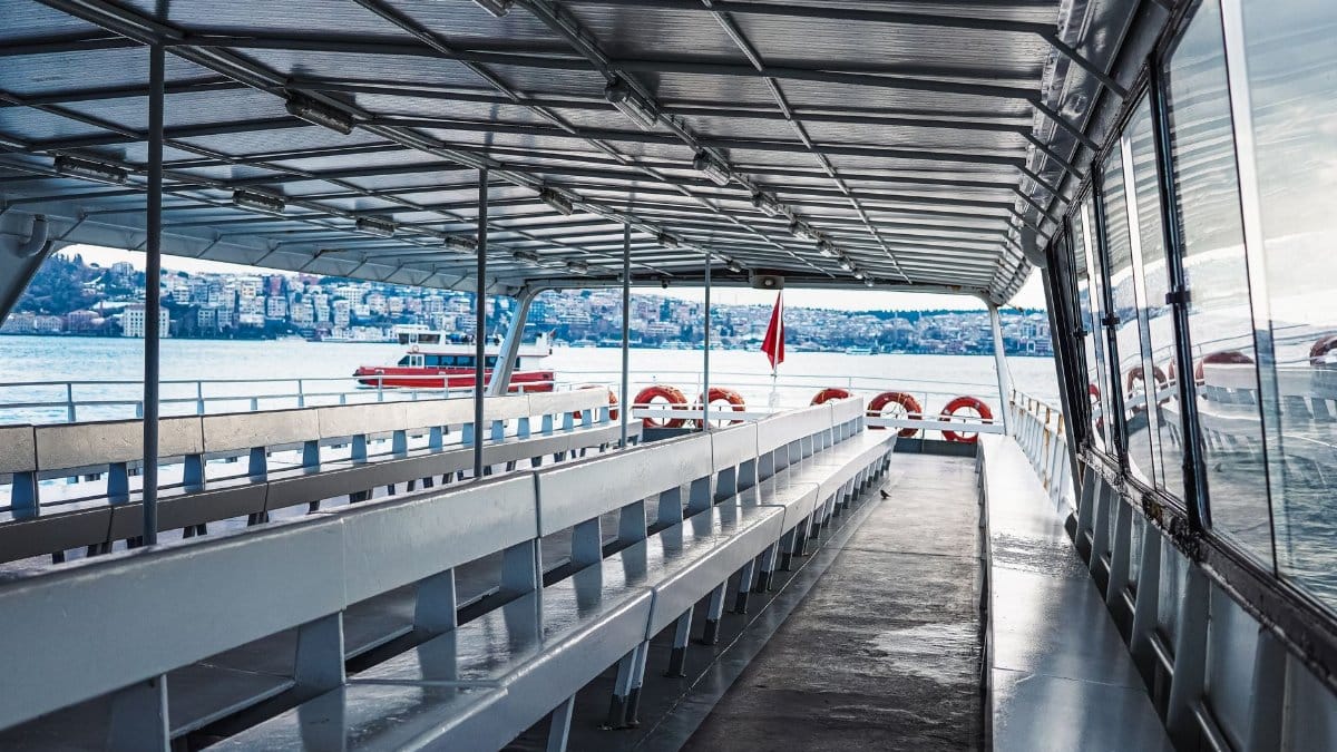 Empty ferry deck with city view, showcasing water and architecture under a covered roof.