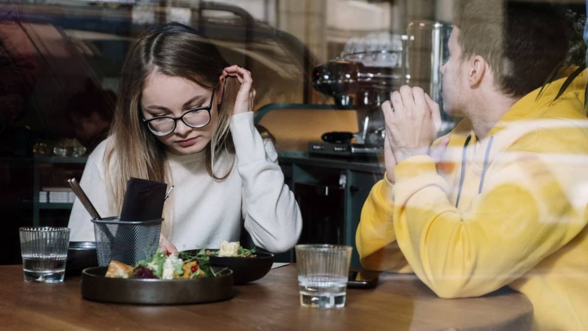 Two friends enjoying a meal at a chic urban cafe, seen through a stylish window.