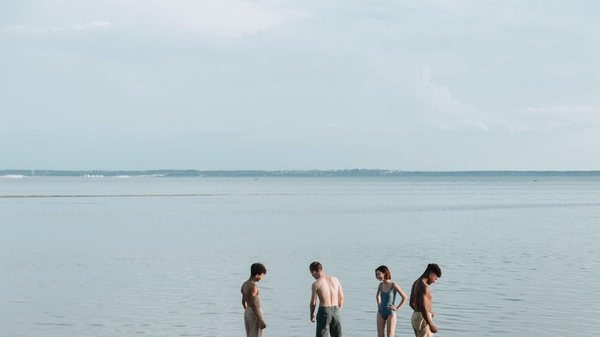 Four friends casually enjoy a warm summer day by the sea, ankle deep in water.