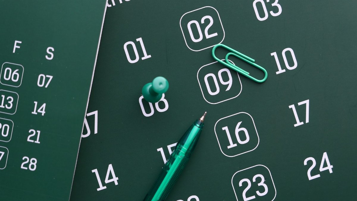 Close-up of a green calendar with pen, push pin, and paper clip for planning and organization.