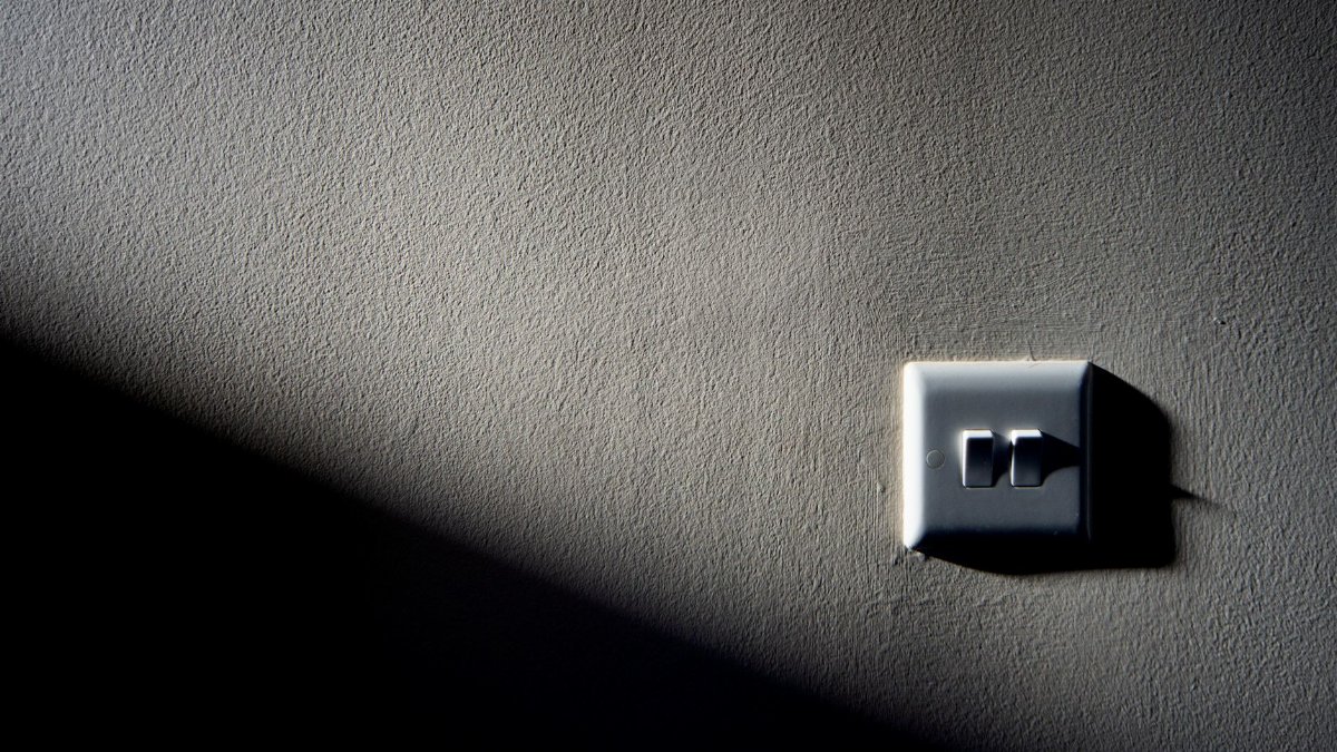 A light switch on a textured wall with contrasting shadow and light, creating a minimalist aesthetic.
