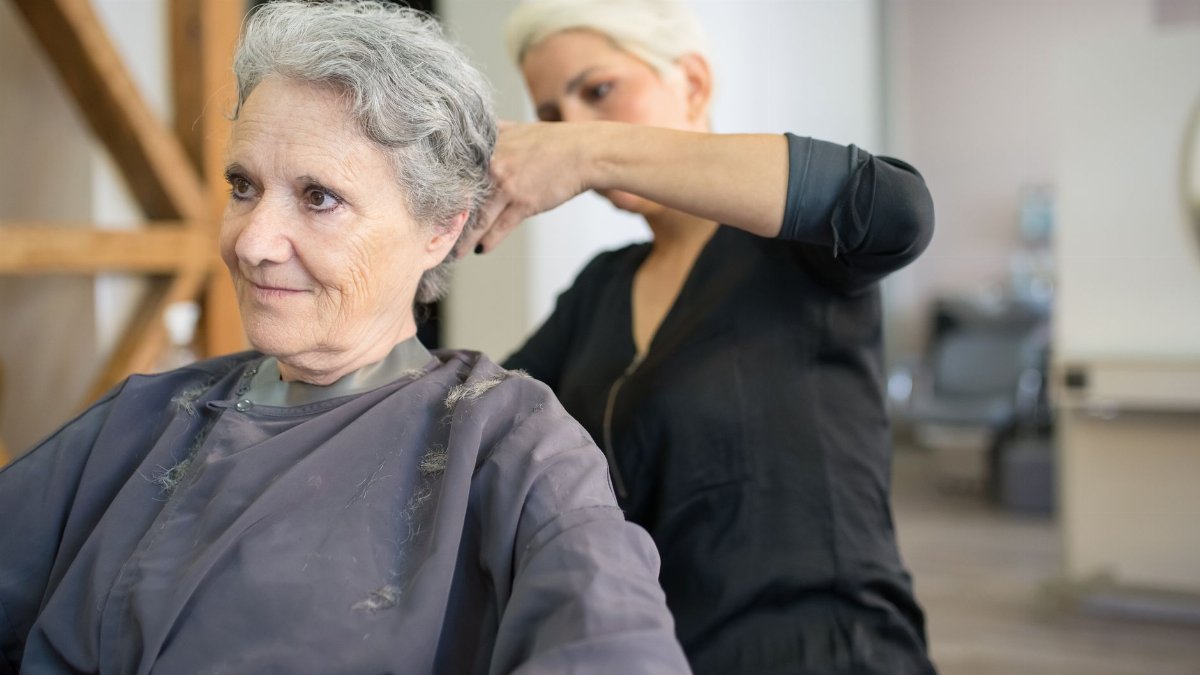 A senior woman receives a haircut at a salon, showcasing a skilled hairstylist in action.