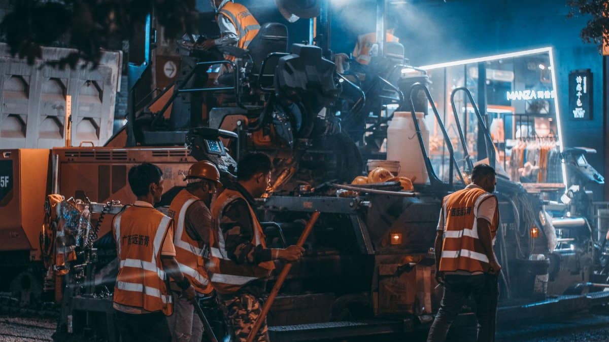 Road construction crew at work with machinery and lights during the night.