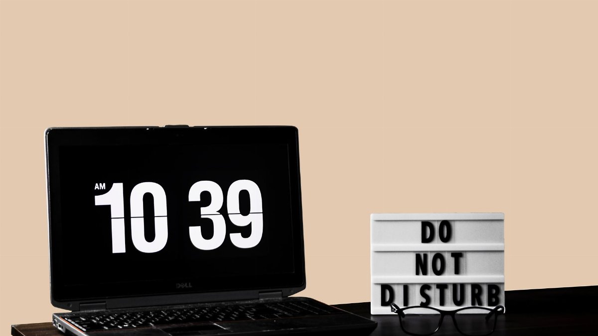 Modern workspace featuring a laptop and 'Do Not Disturb' sign on a wooden desk.