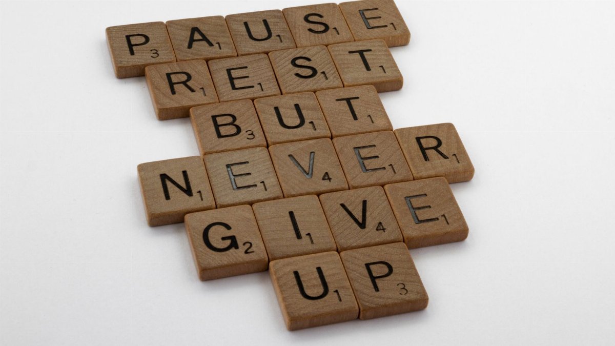 Wooden tiles spelling out 'Pause Rest But Never Give Up' on a white background.
