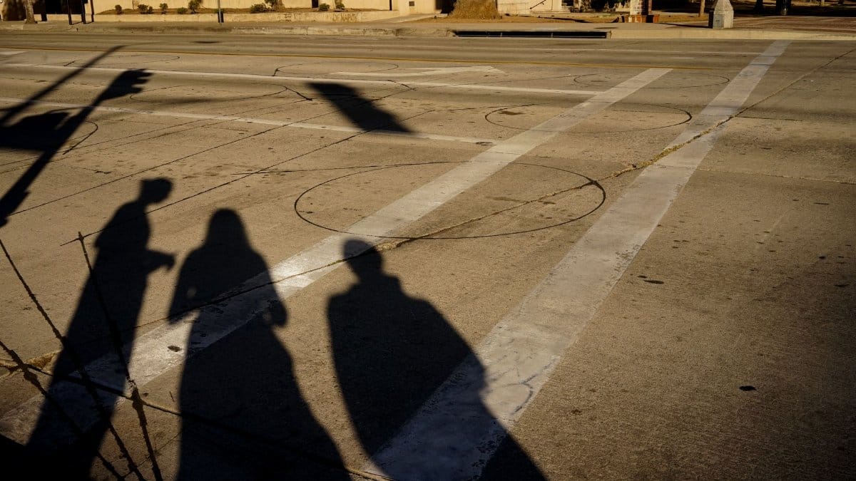Silhouettes of three individuals create dramatic shadows on a city street crosswalk.