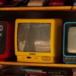 A collection of vintage retro TVs and old telephones on a wooden shelf, evoking nostalgia.
