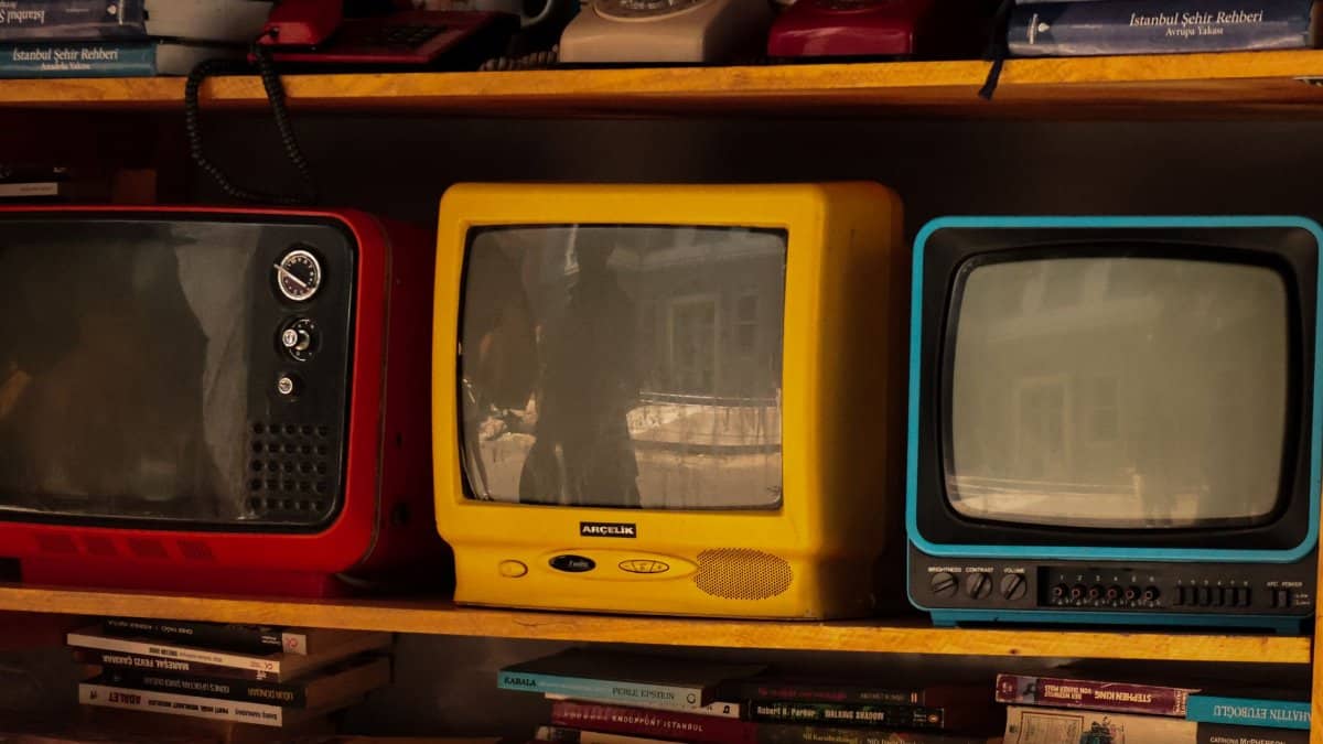 A collection of vintage retro TVs and old telephones on a wooden shelf, evoking nostalgia.