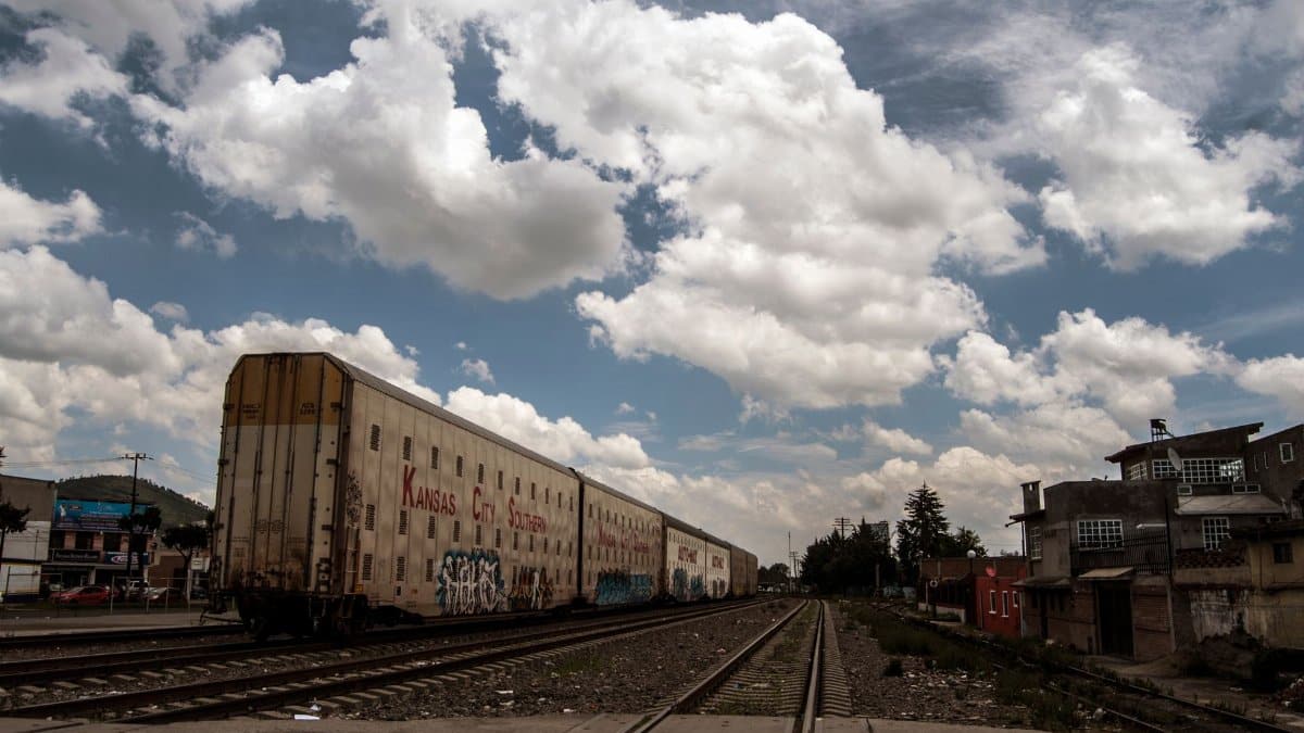 Freight train on tracks with cloudy sky and urban backdrop, captured during daytime.