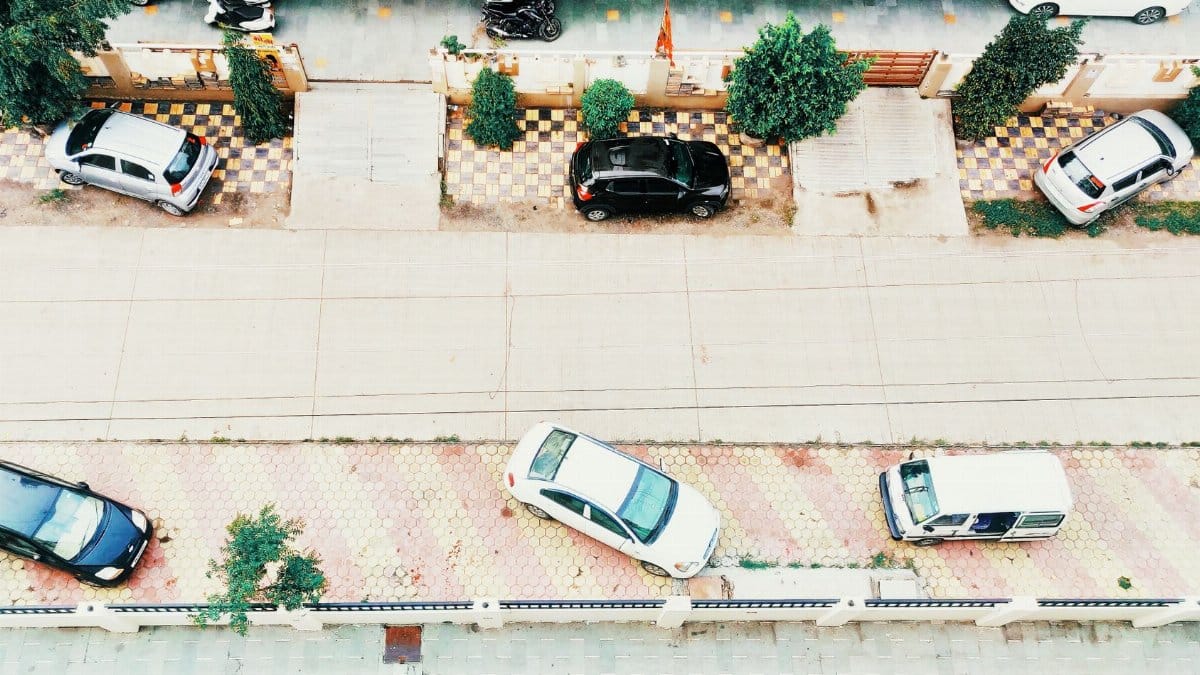 Aerial shot of an urban street in Indore, India, featuring parked cars along a tiled sidewalk and a quiet roadway.
