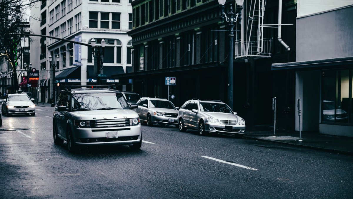 Modern automobiles riding on asphalt roadway near contemporary multistory buildings on street with streetlight and leafless trees in contemporary city