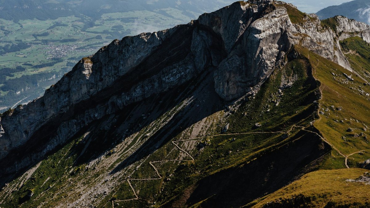 Stunning aerial view of a majestic mountain range with winding trails under a bright sky.