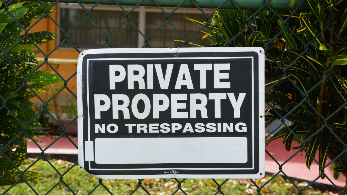 Close-up of a private property no trespassing sign on a chain-link fence with greenery in the background.