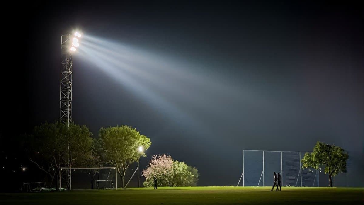 Two people walking on a grass field at night under stadium lights.