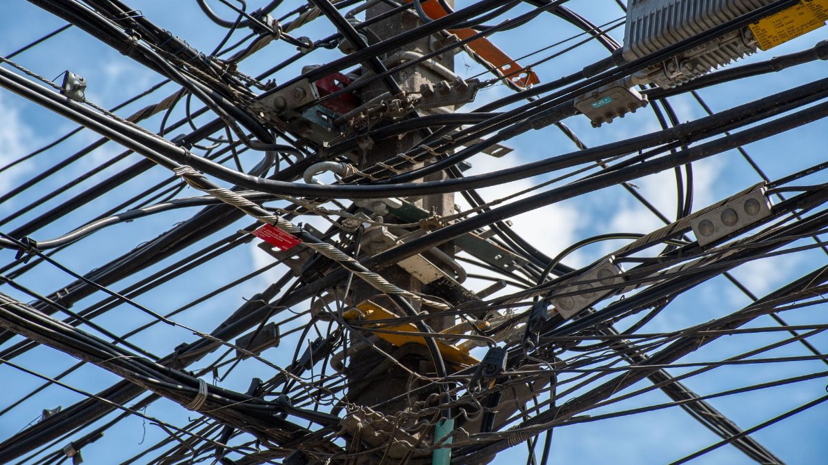 Tangled power lines and cables interwoven on a utility pole in Santiago, Chile against a clear sky.