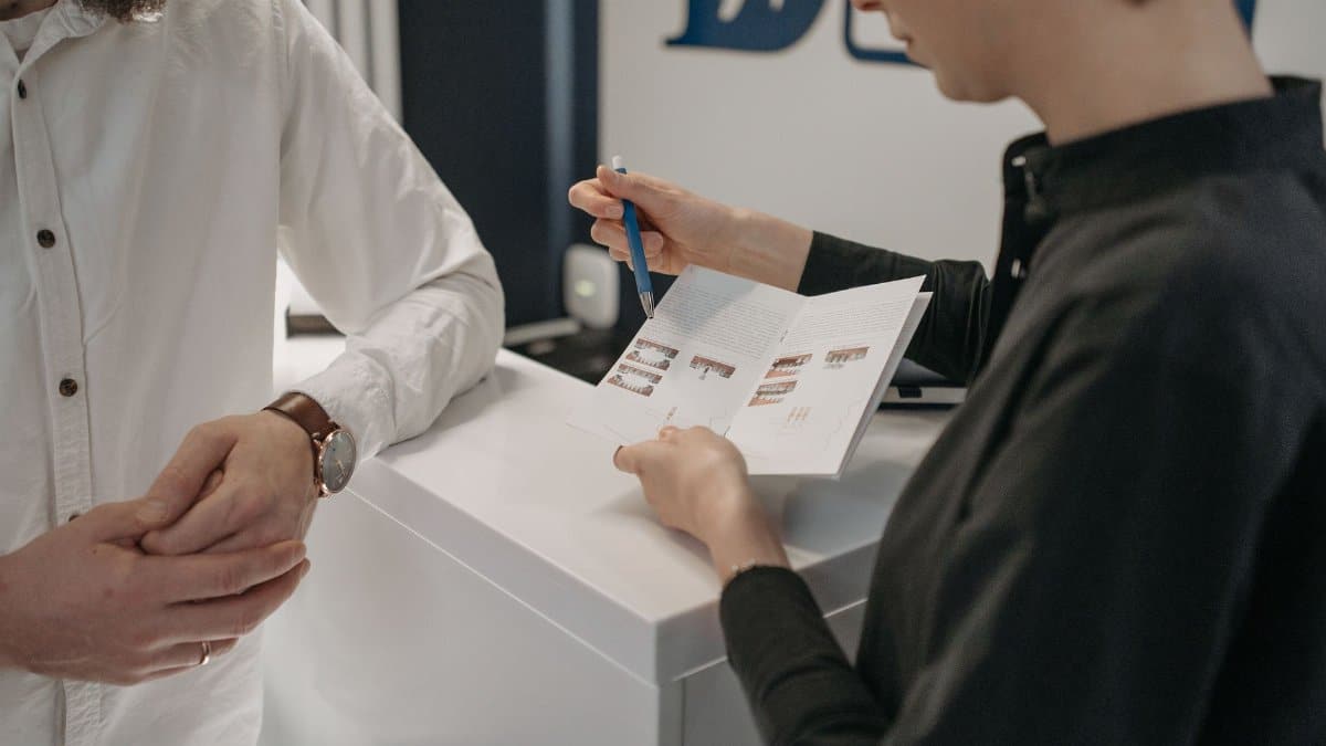 Reception staff explaining information to a customer at a clinic counter.
