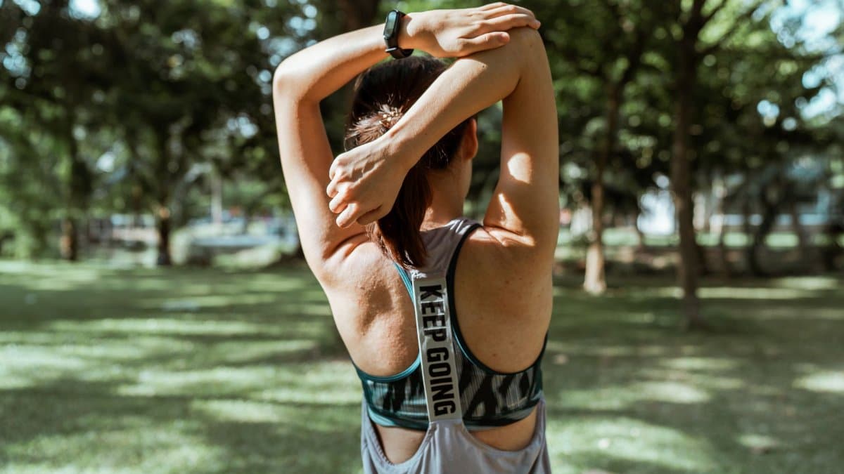 Back view of anonymous sportswoman in activewear doing stretching exercise for back and arms alone in park