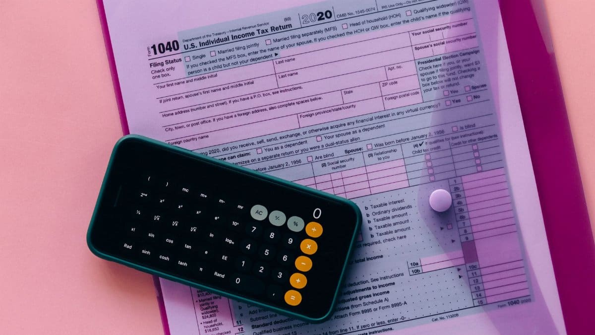 Tax form 1040 with a calculator on a pink background, highlighting finance and accounting themes.
