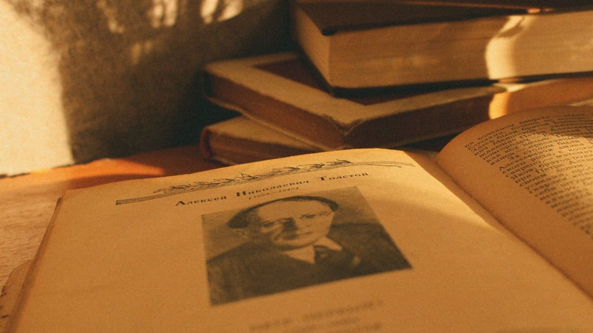 A stack of vintage books in warm sunlight with an open page displaying a portrait.