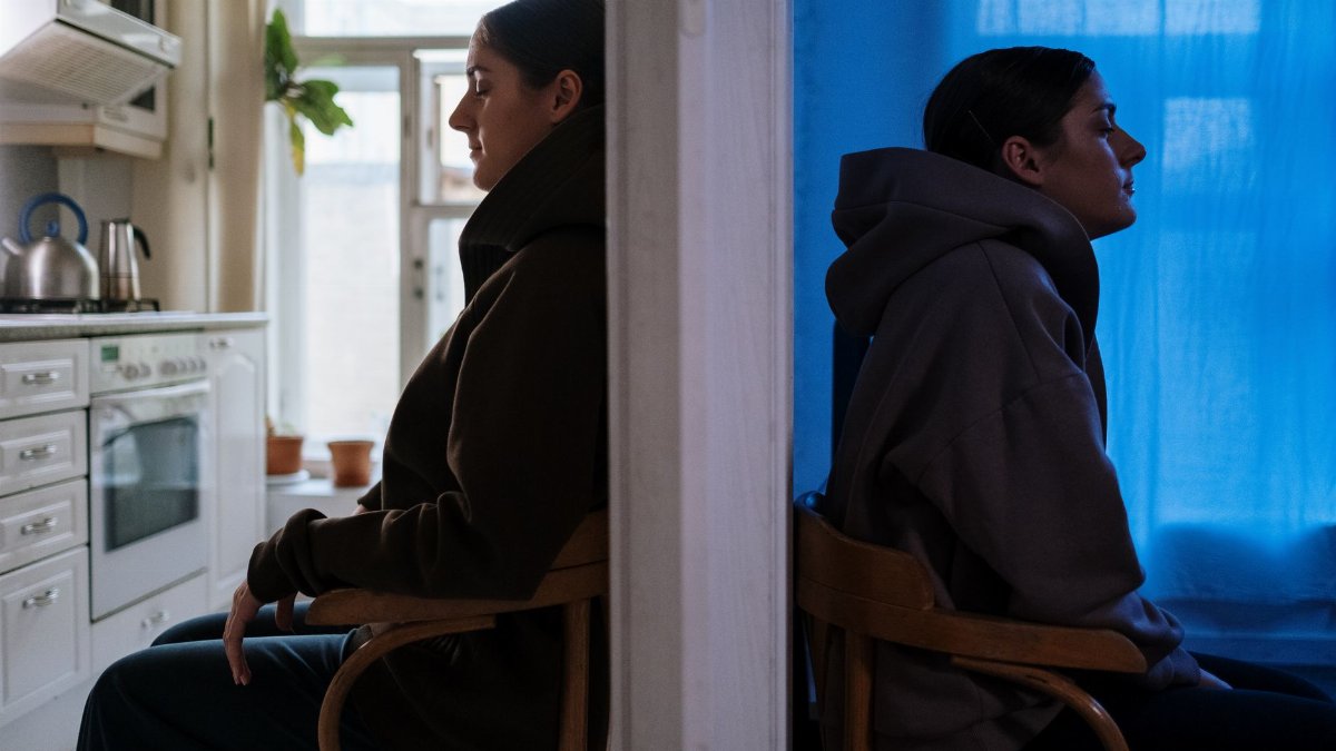 Two women sitting back to back, embodying contrasting emotions in a split room.