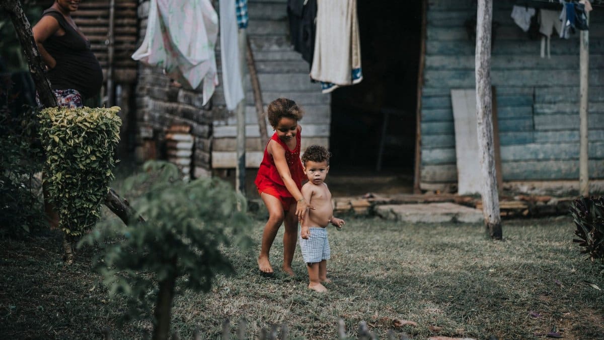 Two children playing outside a rustic house in a rural Cuban setting, showcasing a simple, everyday life moment.