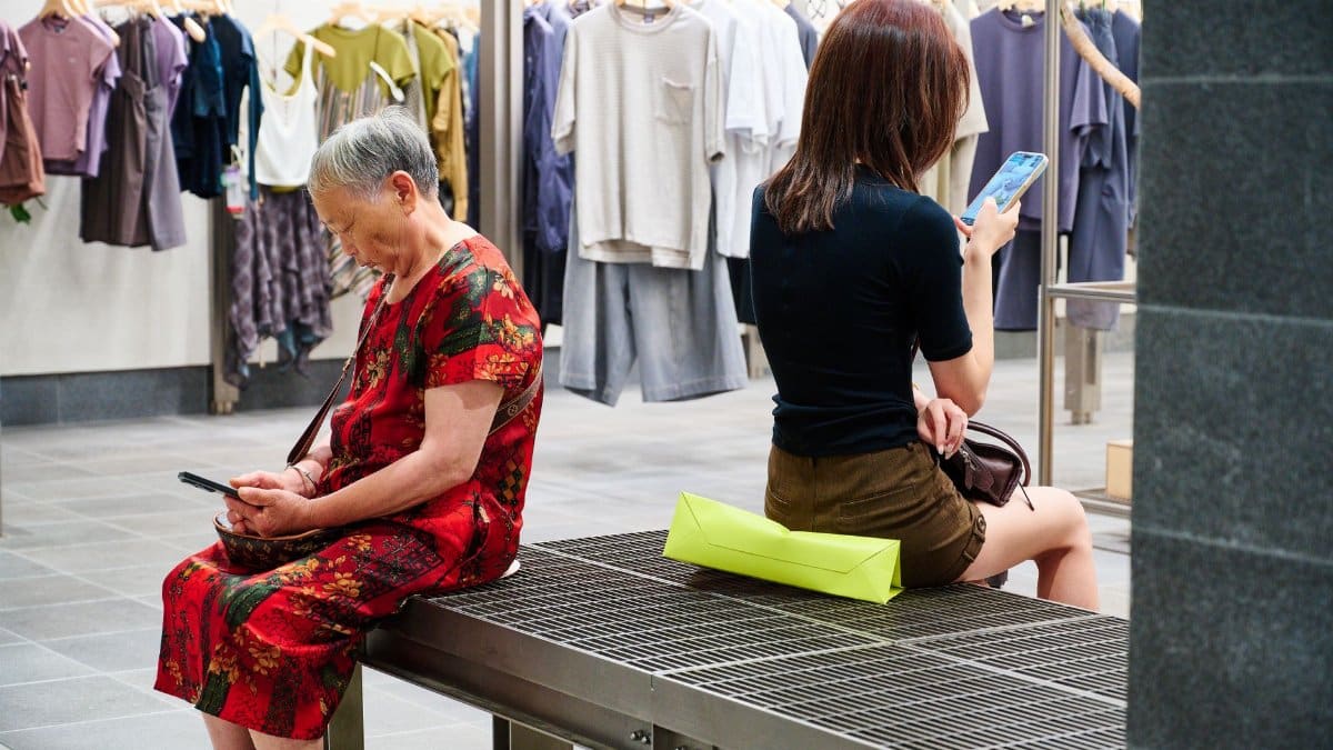 Two women using smartphones in a stylish clothing store setting.